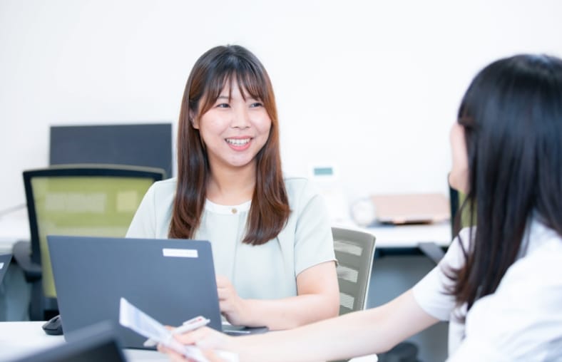 写真：スタッフ2名。顔を見合わせて笑顔を見せている。
